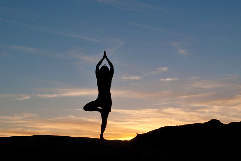 CXECC7 Young gorgeous woman posses with sun salutation Yoga at sunset. Silhouetted agains pale blue dusk sky